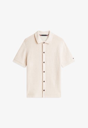 Camisa beige de manga corta con botones y cuello, tela texturizada y pequeño logo en la manga izquierda.
