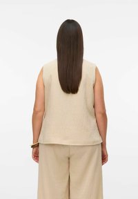 Beige mouwloos topje met een textuurafwerking, gecombineerd met los passende beige broek, gezien vanuit de rug tegen een effen achtergrond.