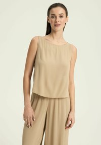 Beżowy bezrękawnik o luźnym kroju, z teksturowanej tkaniny i dyskretnym detalem kieszonki. Minimalistyczny design z okrągłym dekoltem.