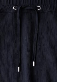 Pantaloni navy in tessuto texturizzato con vita regolabile tramite cordino, caratterizzati da un motivo di tessuto crinkle e occhielli in argento per il cordino.