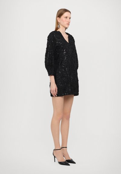 Black sequin dress with a deep V-neck, three-quarter sleeves, and a fitted silhouette; paired with pointed black heels and ankle straps.
