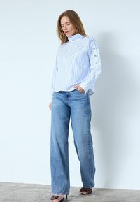 Ljusblå randig blus med lång ärm och hög krage, matchad med vida blå jeans och bruna klackade sandaler.