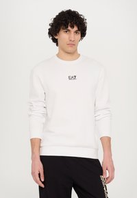 White sweatshirt with round neck and long sleeves, featuring a small black "EA7" logo on the chest. Material appears smooth and soft.