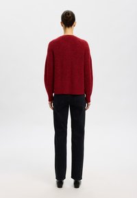 Sarkans adīts džemperis ar garām piedurknēm, īss dizains, teksturēta virsma, kombinēts ar taisnām melnām džinsām un melnām kurpēm.