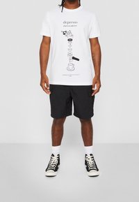 Valkoinen t-paita, jossa on mustia graafikkoja, esittäen kahviin liittyviä kuvastoja ja tekstiä. Yhdistetty mustien shortsejen ja mustien korkeiden tennareiden kanssa.