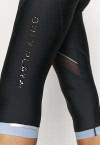Leggings sportivi neri con un logo lucido "ONLY PLAY", pannelli in rete e una fascia in costina blu chiaro. Texture opaca liscia.