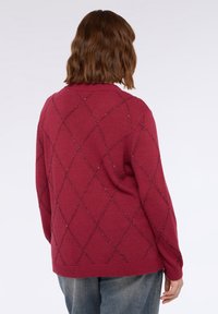 Pulover maron cu un model în diamant accentuat cu o strălucire subtilă. Textură tricotată, cu guler și manșete ondulate, și o croială lejeră.