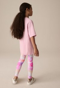 Ružové oversize tričko; farebné legíny s tie-dye vzorom v pastelových odtieňoch ružovej, fialovej a modrej; zdobené biele tenisky s trblietavými doplnkami.