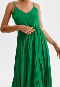 Maxiklänning i livlig grön färg, med ärmlös v-ringning och midjeband. Kjolen har veck för extra textur och flöde.