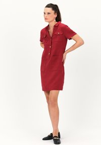 Rotes Leinenhemdkleid mit Kurzarm, zwei Brusttaschen, Knöpfen vorne und geradem Schnitt. Kombiniert mit schwarzen Loafers.