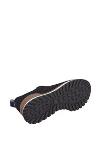 Zapato de ante negro con suela de goma que presenta un agarre texturizado y acentos en beige. La entresuela blanca proporciona contraste. Incluye una pestaña trasera para facilitar el calzado.