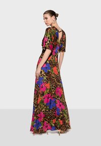 La robe maxi présente un imprimé léopard avec de grands motifs floraux roses, bleus et verts ; elle a des manches courtes et un détail d'ouverture en forme de trou au dos.