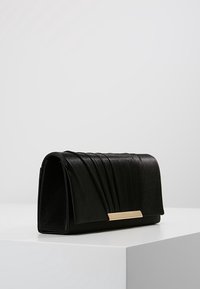 Pochette en cuir noir avec un design plissé, forme rectangulaire et un accent en métal doré à l'avant. Texture lisse, construction solide.