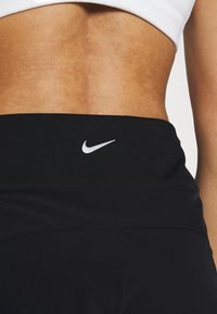 Svarta sportleggings har ett slätt, stretcht tyg med hög midja. En liten vit Nike-logotyp är placerad på midjan.