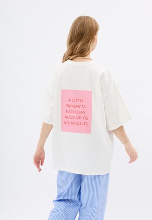 Witte oversized t-shirt met een felroze rechthoekige grafiek op de achterkant met motiverende tekst in vetgedrukte, zwarte letters.