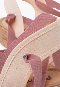 Sandales à lanières en toile de couleur rose pâle et beige, avec une semelle tissée et des accessoires métalliques aux intersections des lanières.