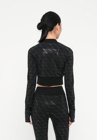 Giacca atletica nera cropped con maniche lunghe, dettagli a motivo romboidale e ampia elastico nera in vita, realizzata in un materiale testurizzato e elastico.