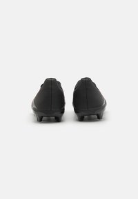 Botas de fútbol negras con un upper texturizado, diseño de perfil bajo y picos de goma para tracción, con un sutil acento rojo en los lados.