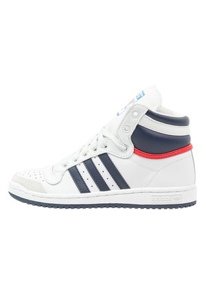 Białe sneakersy Adidas za kostkę z granatowymi paskami, czerwonym akcentem przy pięcie, perforowanym czubkiem i teksturowaną podeszwą.