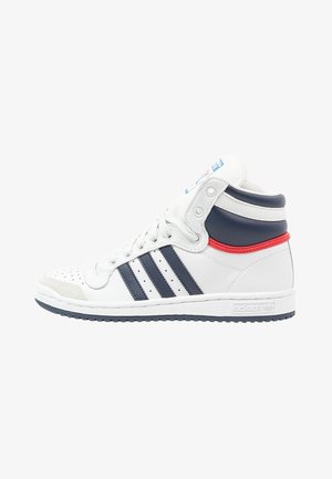 Białe sneakersy Adidas za kostkę z granatowymi paskami, czerwonym akcentem przy pięcie, perforowanym czubkiem i teksturowaną podeszwą.