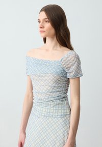 Maglietta a maniche corte, off-shoulder, di colore azzurro chiaro, con texture arricciata e un motivo a quadretti con dettagli crema e azzurro chiaro.