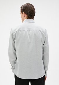 Grijze langwerpige shirt met een standaardkraag, knoopmanchetten en een gladde textuur. Heeft een rechte snit en een detail van rugplooien.