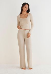 Beige loungewear-set met een langwaardige top met een brede scoop halslijn en losse drawstring-broeken. Zachte, lichte stof, minimalistisch design.