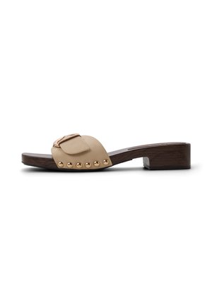 Sandalia beige tipo slide con tachuelas doradas y hebilla en tacón bajo y suela de bloque de madera oscura.