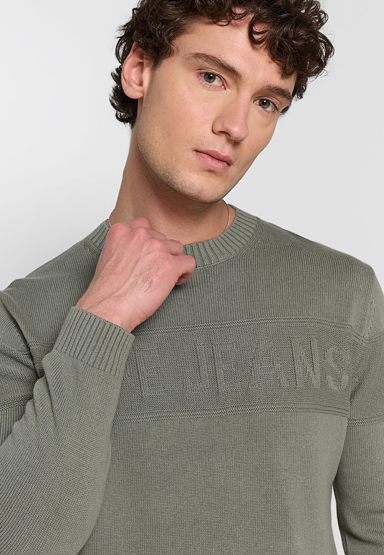 Suéter de punto verde oliva con puños acanalados y cuello redondo, con el nombre de la marca texturizado en el pecho. Material suave, diseño ajustado.