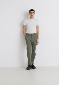 Lightweight olive green trousers with a fitted design, featuring two side pockets and a button closure, paired with a fitted white t-shirt.