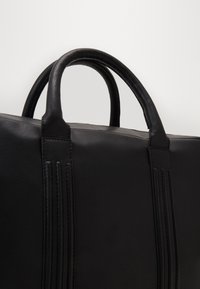 Svart läderväska med två rundade handtag, med vertikala sömdetaljer på sidorna och en slät matta yta.