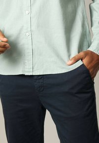 Lichtgroen overhemden met een gestructureerde stof, gecombineerd met marineblauwe broeken met zijzakken en een gladde afwerking.