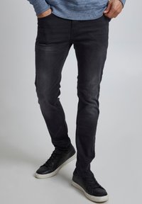 Svarta skinny jeans med en blekt finish, tillverkade av denim. Bärs med svarta sneakers som har vita sulor. Texturerad tyg synlig.