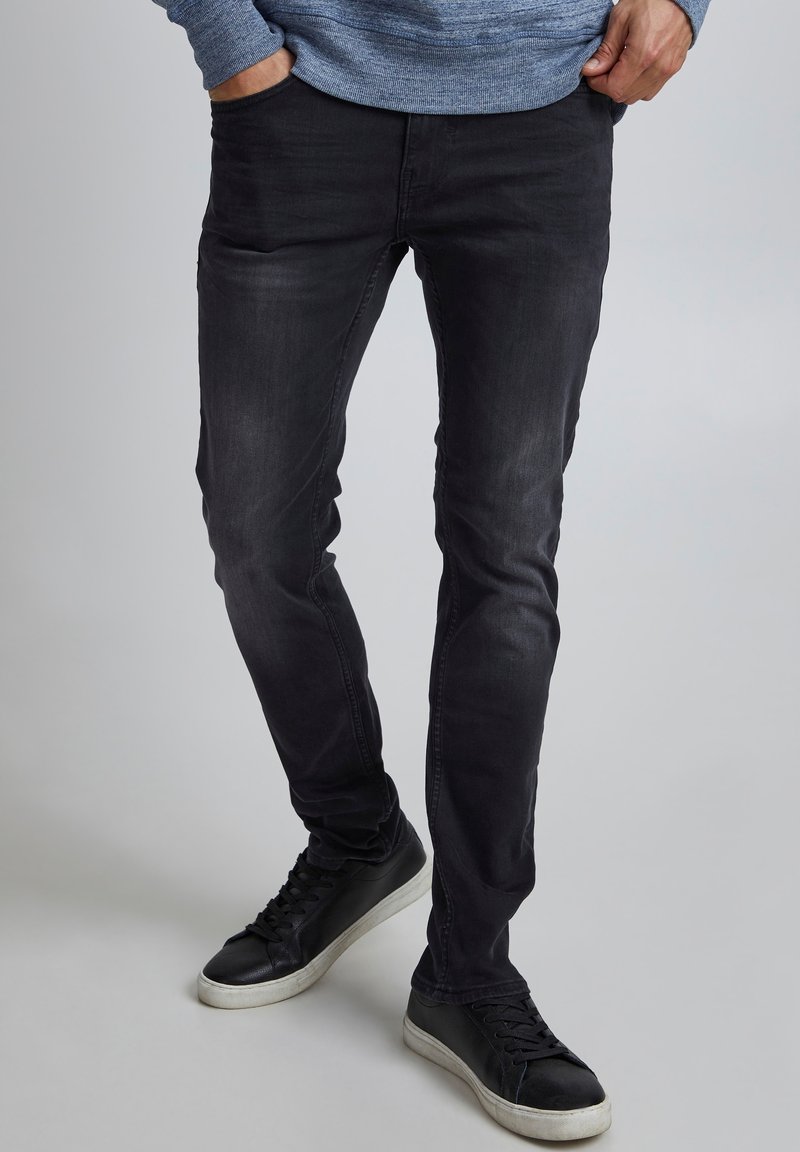 Svarta skinny jeans med en blekt finish, tillverkade av denim. Bärs med svarta sneakers som har vita sulor. Texturerad tyg synlig.