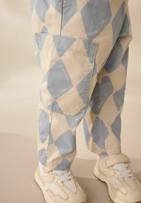 Los pantalones a cuadros en azul claro y crema cuentan con un bolsillo lateral, combinados con zapatillas deportivas en beige y blanco con detalles de malla.