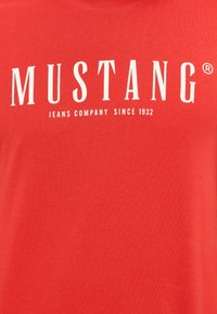 Czerwony bawełniany t-shirt z białym logo "MUSTANG" oraz podpisem "JEANS COMPANY SINCE 1932" poniżej. Gładka faktura, krótkie rękawy, okrągły dekolt.