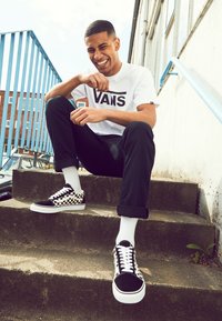 Sorte og hvide Vans sneakers med ternet mønster, parret med hvide sokker, sorte bukser og en hvid Vans logo t-shirt.
