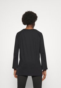 Czarna tunika z długim rękawem, o zaokrąglonym dole i rękawach raglanowych. Wykonana z gładkiej, elastycznej tkaniny. Minimalistyczne detale z tyłu.