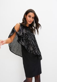 Abito nero con sovrapposizione di paillettes, caratterizzato da un design fluido, spalle scoperte e una texture liscia. Il colore nero domina l'insieme.
