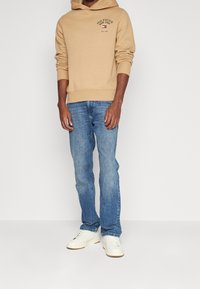 Felpa con cappuccio beige con logo "HILFIGER NEW YORK", abbinata a jeans azzurri e sneaker bianche. Look casual e comodo.