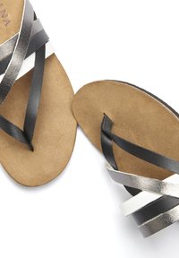 Sandales strappy noires, argent métallisé et blanches avec un semelle plate en cuir marron et des brides tissées. Design minimaliste, style ouvert à l'avant.