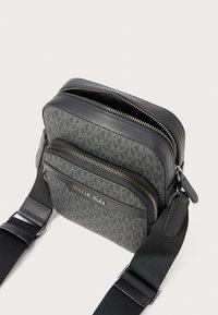 Borsa crossbody nera e grigia con motivo a monogramma, cerniere doppie, dettagli in pelle e tracolla regolabile. Tessuto testurizzato e accessori in metallo.