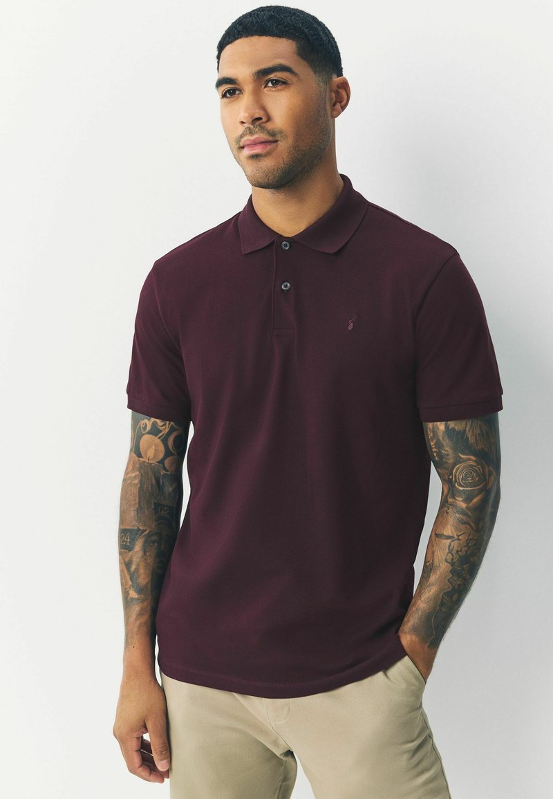 Burgundy-paitainen polo-paita, joka on valmistettu puuvillasta. Paita on slim fit -mallinen, lyhythihainen, kahdella napilla varustettu nappilista ja siinä on hillitty logodetail rintakehässä.