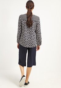 Camisa de manga larga a rayas en blanco y negro con un reverso sólido negro texturizado, combinada con culottes de longitud a la rodilla en color navy y zapatos negros de deslizar.