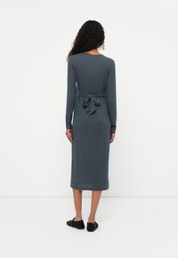 Siva pletena obleka z dolgimi rokavi, z vezanim pasom in dolžino midi, v kombinaciji s črnimi strukturiranimi čevlji.