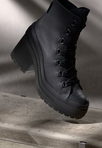 Bottines à talons hauts en cuir noir avec une finition texturée, un laçage à l'avant et une semelle en caoutchouc avec un bord s'ornant d'un motif.