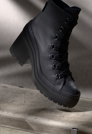 Bottines à talons hauts en cuir noir avec une finition texturée, un laçage à l'avant et une semelle en caoutchouc avec un bord s'ornant d'un motif.