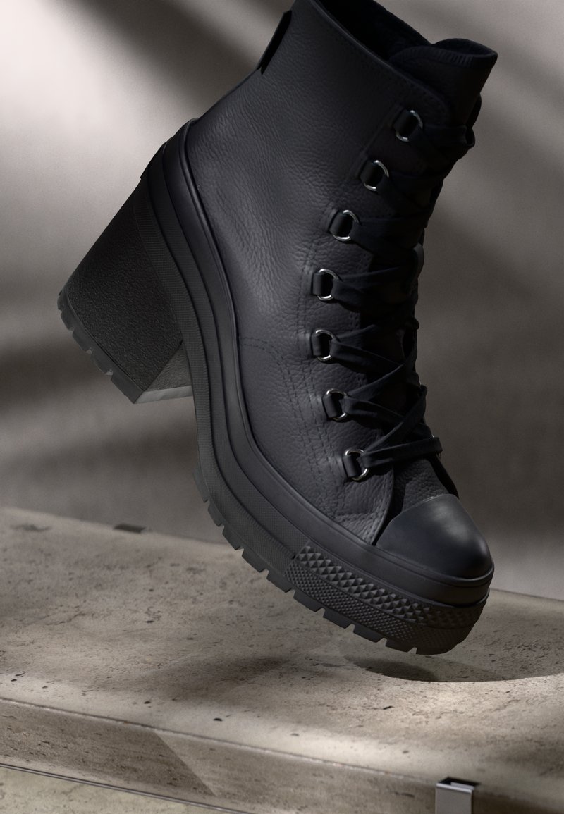 Bottines à talons hauts en cuir noir avec une finition texturée, un laçage à l'avant et une semelle en caoutchouc avec un bord s'ornant d'un motif.