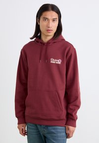 Hanorac capotat maroon, cu buzunar frontal, manșete ribate și un logo brodat cu "Dickies Donut House" în culoare deschisă.