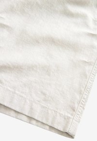 Gros plan sur un tissu en lin beige montrant des détails de couture de l'ourlet et la texture.